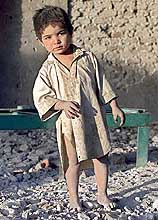 A young Afghan refugee stands in the rubble of a house