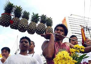 A man runs an iron rod with pineapples through his cheek