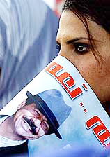 An Iraqi girl cover her face with a picture of President Saddam Hussein