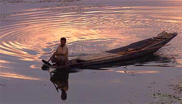 A Kashmiri fisherman rows his boat as the sun sets over Dal Lake