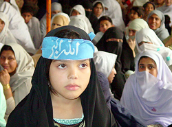 A Pakistani girl wearing a head band, which reads "God is great," listens to speeches