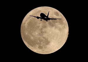 An airliner is silhouetted against a full moon