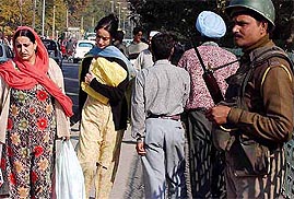 Kashmiri women walk past an alert security man