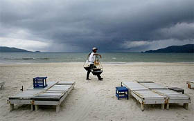 A Thai food vendor strolls past empty beach chairs