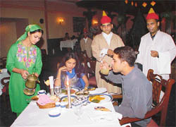 A waiter dressed in Kashmiri attire serving kahwa in a samovar to the guests at the Kashmiri Food Festival