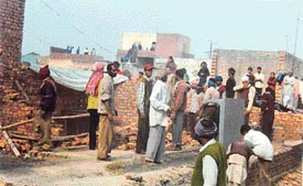 Residents collect their belongings as JCB machines raze illegal structures to the ground in Baba Jiwan Singh Nagar 