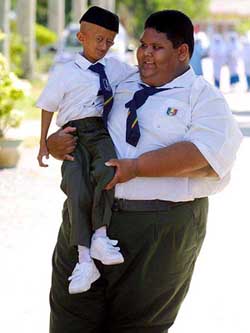 Mohamad Muaz sits in the arms of his schoolmate Mohamad Anuar as they go to school in Kedah, Malaysia, on Tuesday.