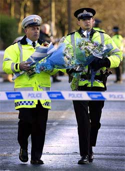 Police officers carry flowers on Wednesday to the scene where Detective Constable Stephen Oake
