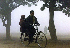 Commuters bicycle through thick fog