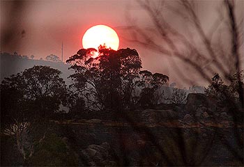 A red sun rises over the fire-torn Canberra suburb of Rivett