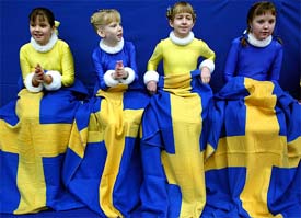 Flower girls warm themselves under Swedish flag blankets during the first day of the European Figure Skating Championships