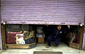 A Kashmiri shop owner looks through half-shut shutters