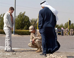 US military police and a Kuwaiti investigator look at blood stains on a road where unknown attackers ambushed and shot dead a U.S. defense department civilian employee 
