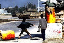 Palestinian boys throw stones while an Israeli tank and military bulldozer raid into Beit Hanuo town