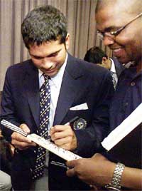Sachin Tendulkar signs a cricket bat as Zama Ndamane watches during his team's arrival at Johannesburg International Airport