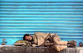 A homeless man sleeps in front of a closed shop