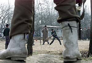 A soldier stands guard as children play cricket
