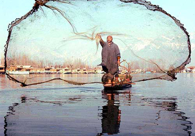 A fisherman spreads the net in swollen Dal Lake