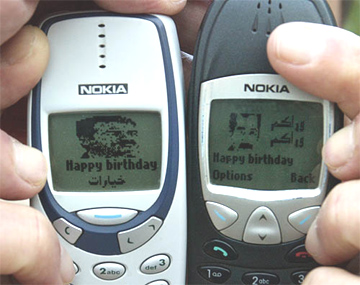A Jordanian man holds mobile phones, depicting images of ousted Iraqi President Saddam Hussein with the message 'Happy birthday'
