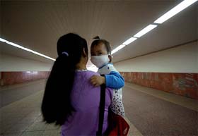 A child wears a mask as she is carried by her mother at a passageway under Tiananmen Square in Beijing 