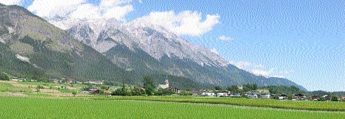 A panoramic view of Austrian landscape, with the mighty Alps towering over lush fields of a rural habita