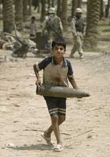 A young Iraqi boy carries a US-made 155-mm shell during a cleanup operation in Baghdad