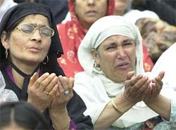 Kashmir women pray as a supporter showers petals