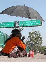 With mercury soaring, a beggar seeks alms under an umbrella