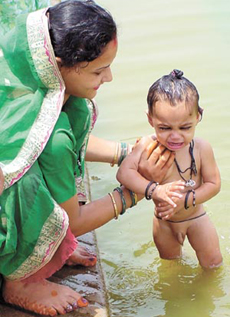 A mother bathing her child on the occasion of Guru Arjan Dev's Martyrdom Day at Gurdwara Bangla Sahib Sarovar in the Capital on Monday.