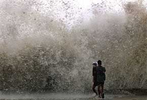 Two boys run towards a huge wave