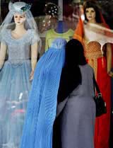 Veiled Afghan women look at western dresses displayed at a shop in Kabul