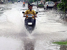 A scooterist passes through a waterlogged road