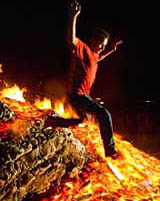 A young man jumps over a giant bonfire
