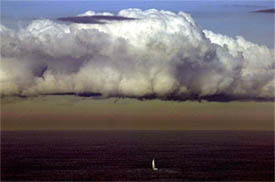 A small sailing boat heads out to sea as a pollution haze hangs underneath a large storm cloud at the east of Sydney Harbour's headlands