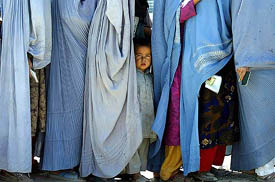 An Afghan boy stands next to his widowed mother as she, along with other widows,  wait in a queue of war widows to receive their monthly ration from the CARE International organisation