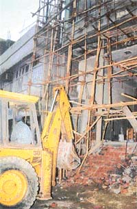 A bulldozer pulls down parts of supporting pillars of a commercial building under construction
