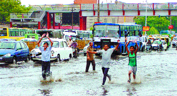 Children wade through a waterlogged road, unmindful of the traffic snarls in the city. 