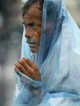 A pedestrian covers himself with a plastic sheet during a monsoon rain