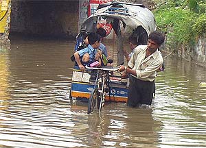 A rickshaw-puller, carrying schoolchildren, wades through rainwater