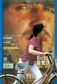 A Chinese woman pushes a bicycle past a poster of newly signed Real Madrid player David Beckham