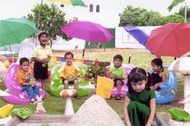 Children of Chanda Mama Play School, Green Enclave, play with sand and seated under colourful umbrellas enjoy
