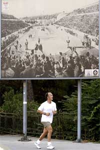 A man jogs past a poster depicting Athens' Panathenean Stadium, venue of the first modern Olympics, held in 1896