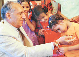 A girl from an orphanage ties a rakhi on the wrist of the UT Administrator