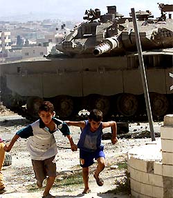 Palestinian boys run away after throwing stones at an Israeli tank during an army operation in the West Bank city of Jenin
