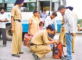 Police personnel check the bag of a passenger at the inter-state bus terminus