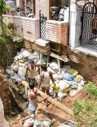 Labourers repair road in front of two houses