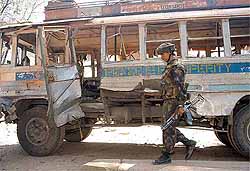 An Army jawan inspects a damaged bus