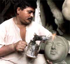 An artisan uses a bowler lamp to dry an idol of Goddess Durga 
