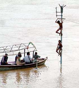 A relief boat tries to rescue two kids who climbed on a pole to save themselves from flood