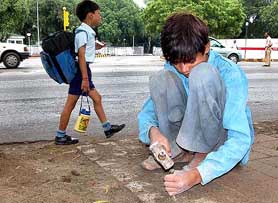 A schoolkid walks past a child who is busy working on a pavement